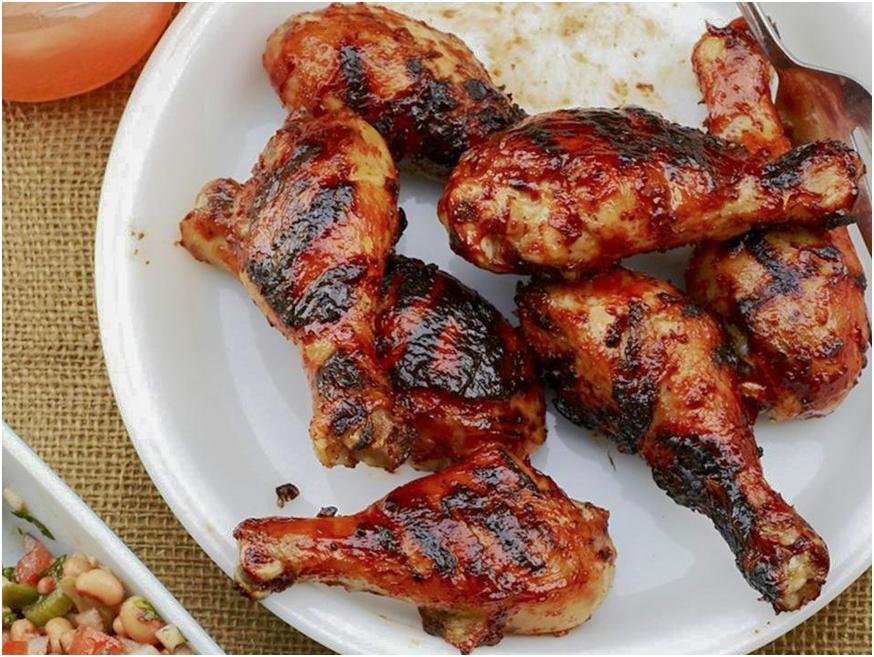 Plate of grilled barbecue chicken drumsticks with a smoky, charred glaze served on a white dish